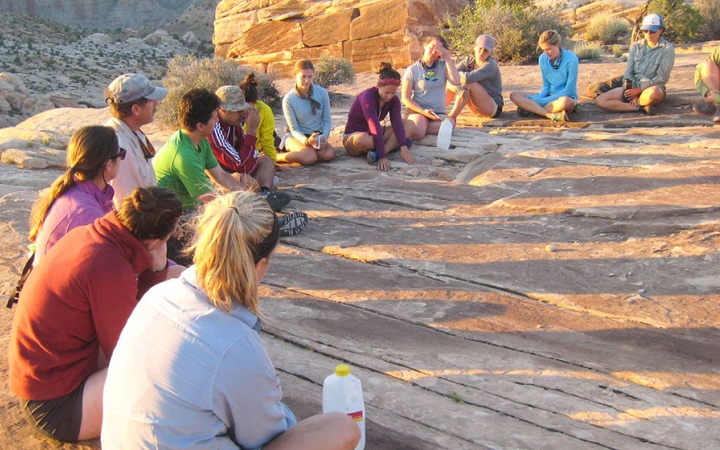 A group of people sit in a circle in a desert landscape